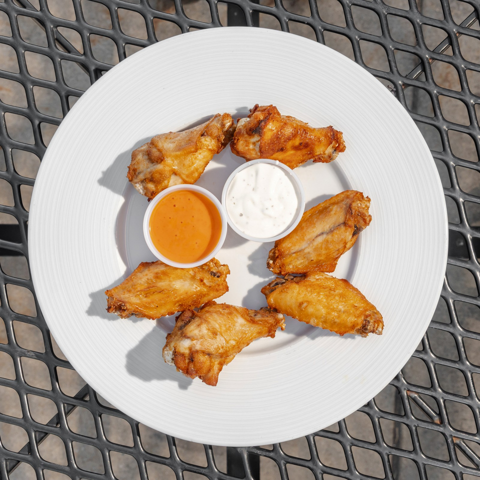Crispy chicken wings arranged around cups of orange hot sauce and creamy ranch dressing on a white plate.